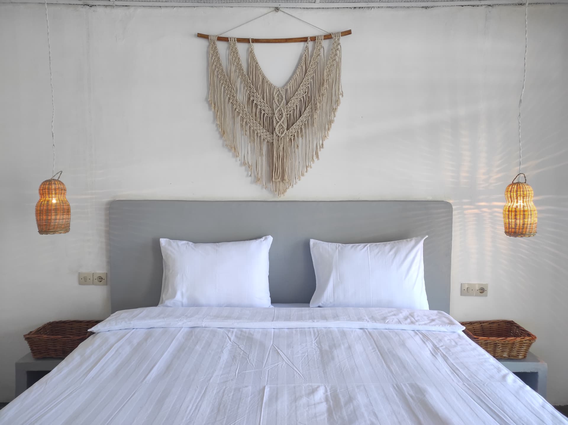 Double bed with macramé wall hanging and rattan bedside lamps